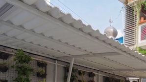 Un espacio al aire libre techado con una moto estacionada bajo un toldo blanco, rodeado de plantas en macetas.