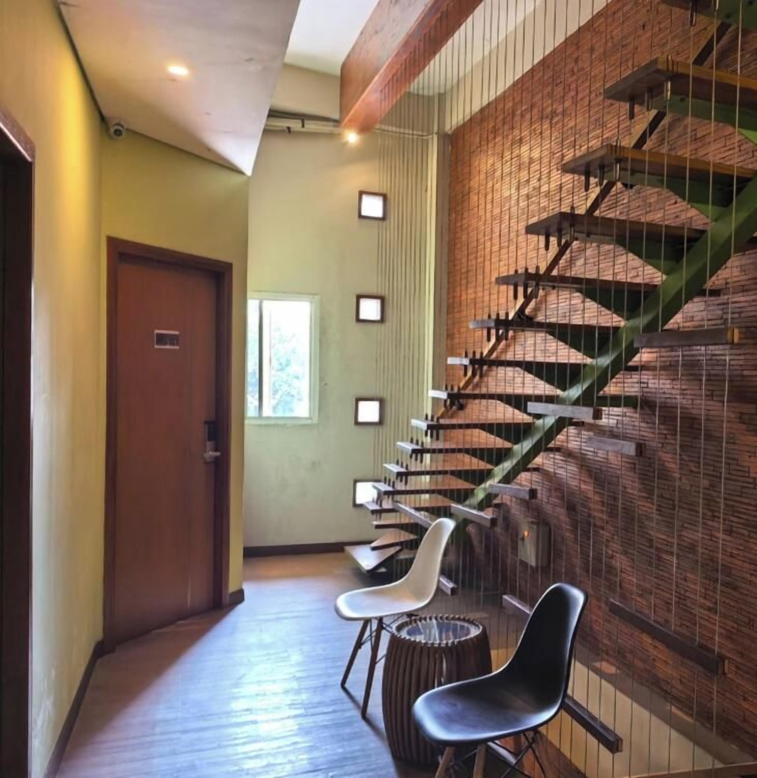 A hallway with a wooden floor, a staircase with a green handrail, and two chairs.