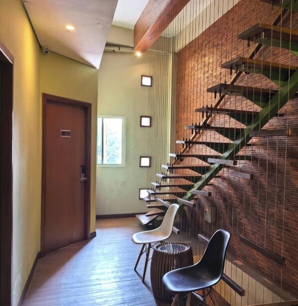 A hallway with a wooden floor, a staircase with a green handrail, and two chairs.