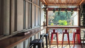 Un largo banco con techo de listones de madera y ventana con vista a un jardín.