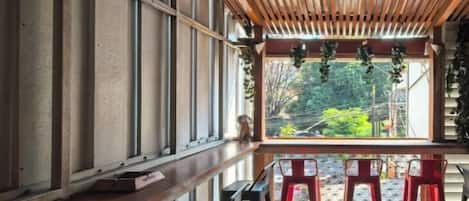 Un largo banco con techo de listones de madera y ventana con vista a un jardín.