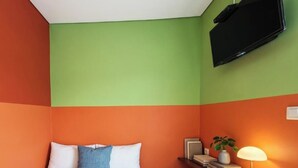 Una habitación con una cama, un televisor montado en la pared y una mesita de noche con una lámpara.