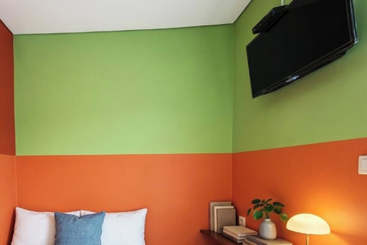 Una habitación con una cama, un televisor montado en la pared y una mesita de noche con una lámpara.