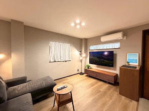 Ein modernes Wohnzimmer mit Fernseher, Sofa, Couchtisch und einer kleinen Kommode.