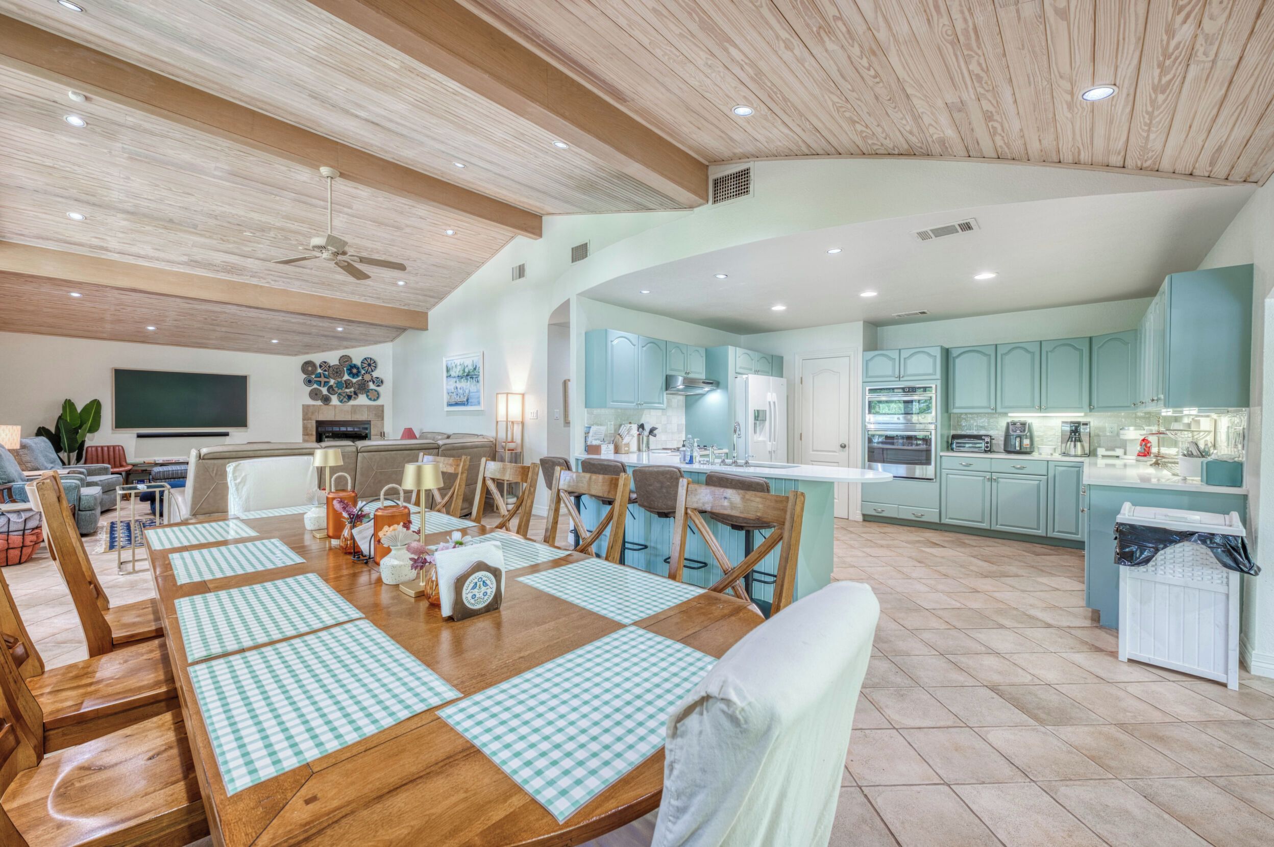 A spacious living area with a dining table set for four, a kitchen with light blue cabinets, and a ceiling fan.