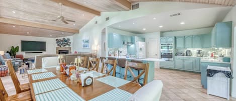 A spacious living area with a dining table set for four, a kitchen with light blue cabinets, and a ceiling fan.