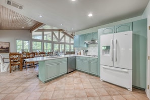 Une cuisine spacieuse avec un grand îlot central, des meubles de couleur vert clair et un réfrigérateur blanc.