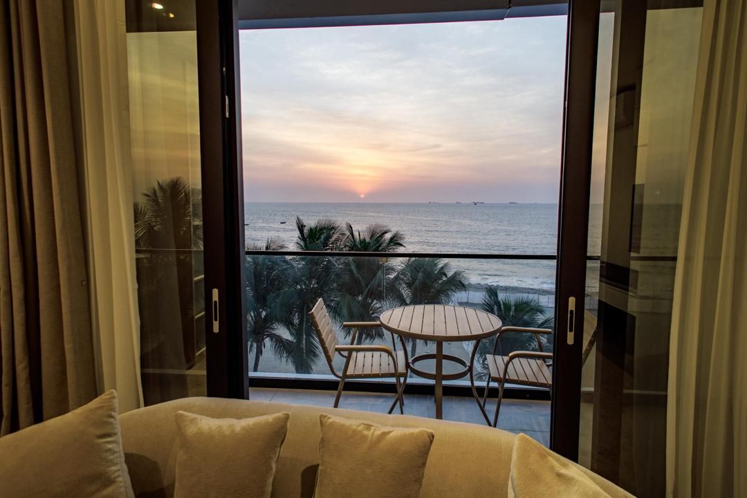 Un balcón con vista al mar al atardecer, una mesa redonda de madera y dos sillas.