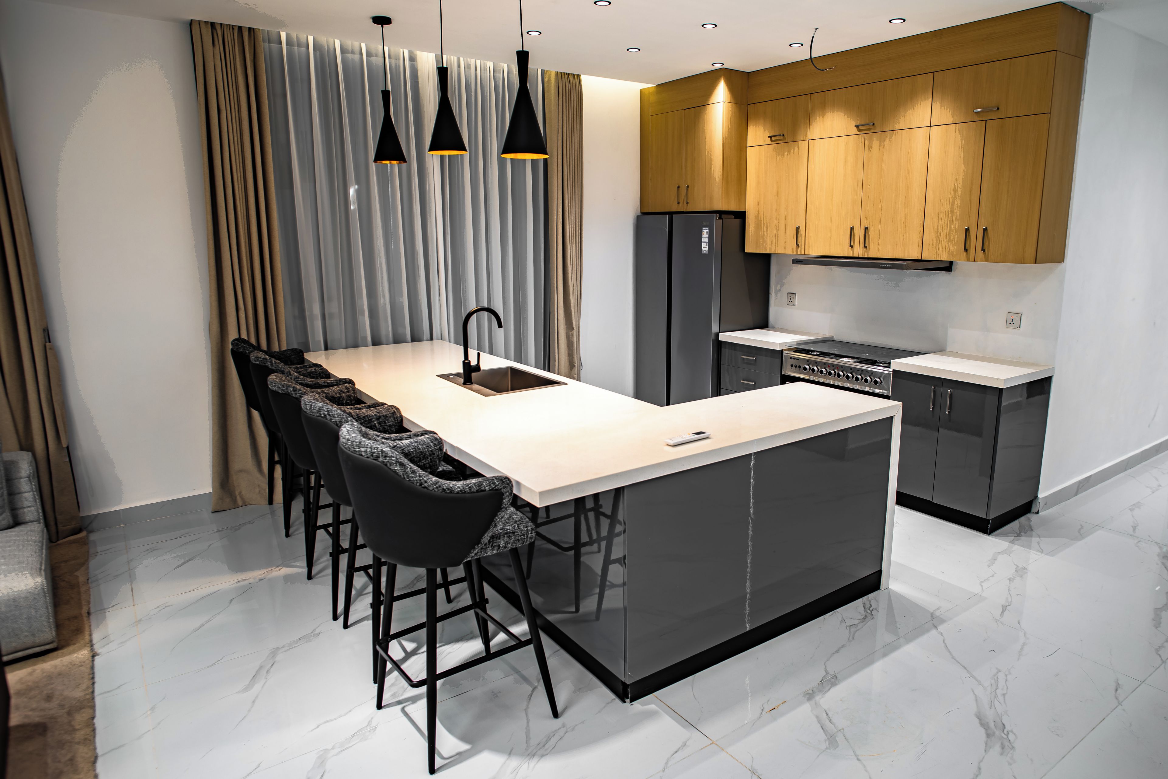 Una cocina moderna con una isla central, taburetes negros, horno empotrado y armarios de madera.