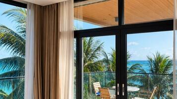 A modern hotel room with a large sliding glass door leading to a balcony with a view of palm trees and the ocean.