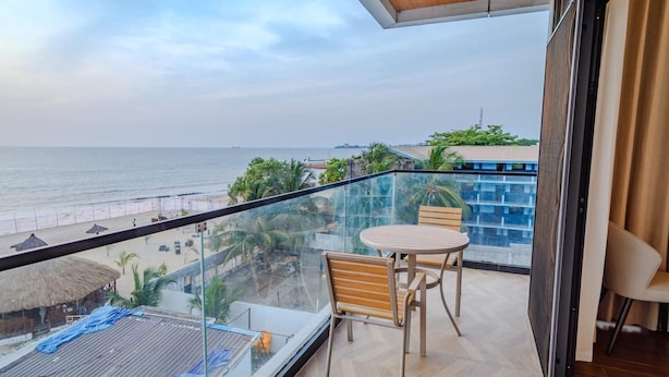 Een balkon met uitzicht op het strand, een tafel en stoelen.