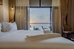 A hotel room with a bed, a chair, a small table, and a view of the sea through a large window. - TJ Tower (Freetown)