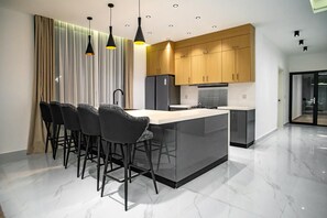 Una cocina moderna con una isla central, taburetes de bar, armarios de madera e iluminación colgante.
