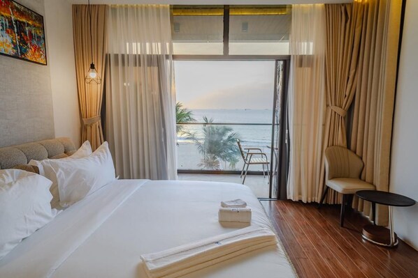 Habitación de hotel con cama, una silla, una mesita y vistas al mar desde un balcón.