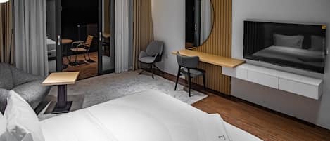 A modern hotel room with a bed, a desk, a chair, a large mirror, and a television.