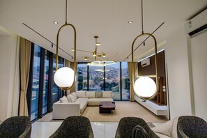 Una habitación de hotel moderna con un ventanal grande, un sofá, una mesita de centro y un rincón de estar con sillones.