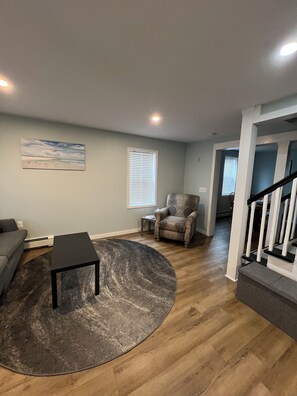 A living room with a gray couch, a black coffee table, and a patterned armchair.
