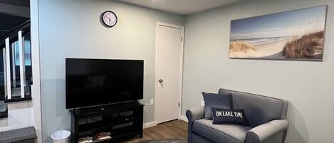 Una sala de estar con una televisión de pantalla plana, un sofá gris, un tapete grande y un cuadro en la pared.