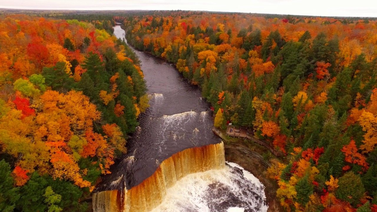 A waterfall surrounded by dense forest with autumn foliage.