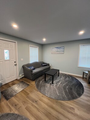 A living room with a gray sofa, a black coffee table, a gray rug, and a door with a stained glass window. - "Twin Haven Manistique 4BR Retreat" (Manistique)