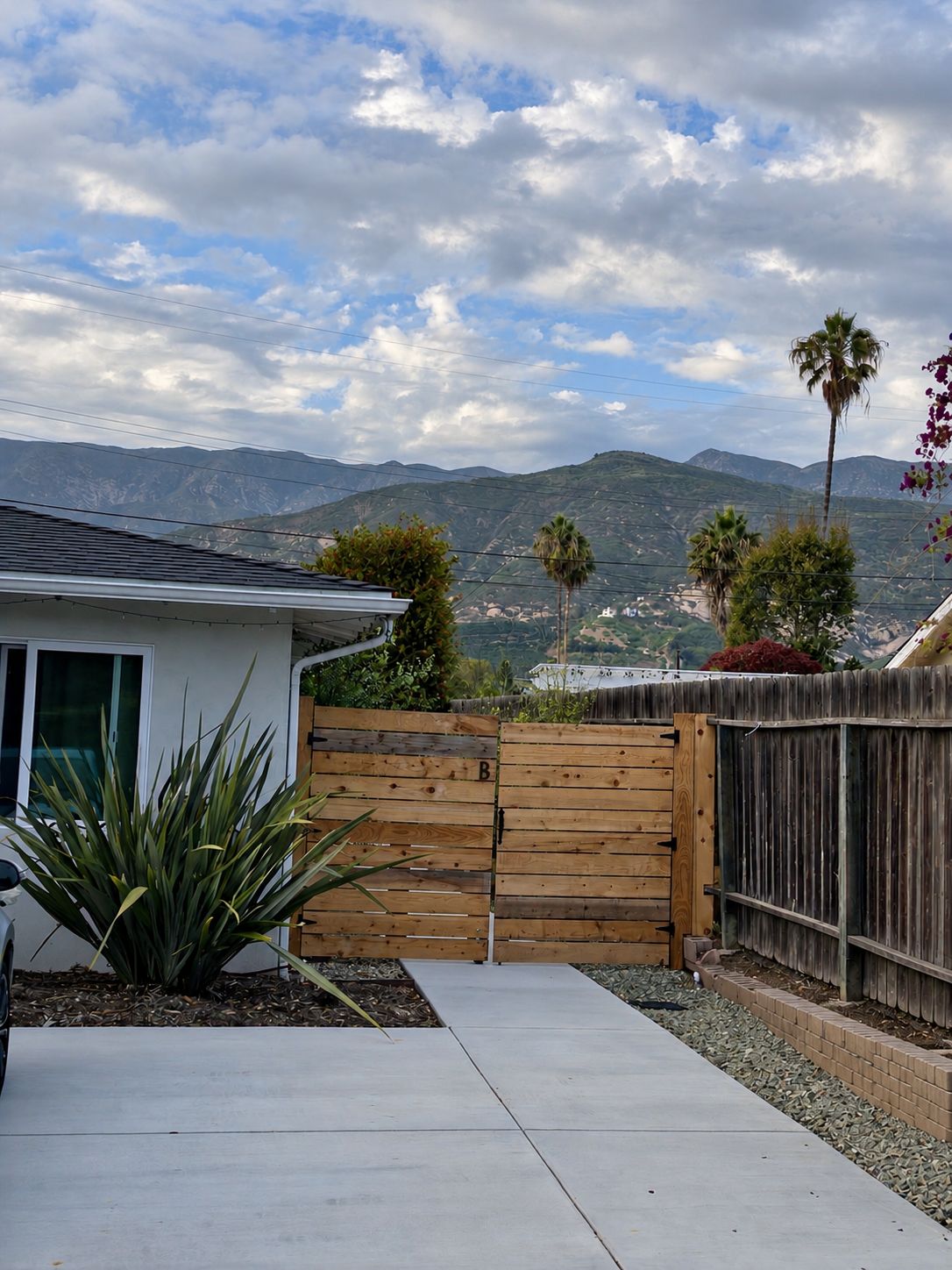 A residential backyard with a wooden fence, a patio, and a view of mountains.