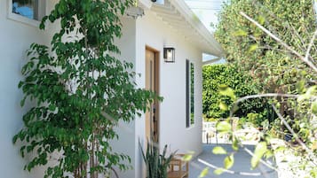 Una casa de exterior blanco, una puerta de madera y una planta en maceta en primer plano.