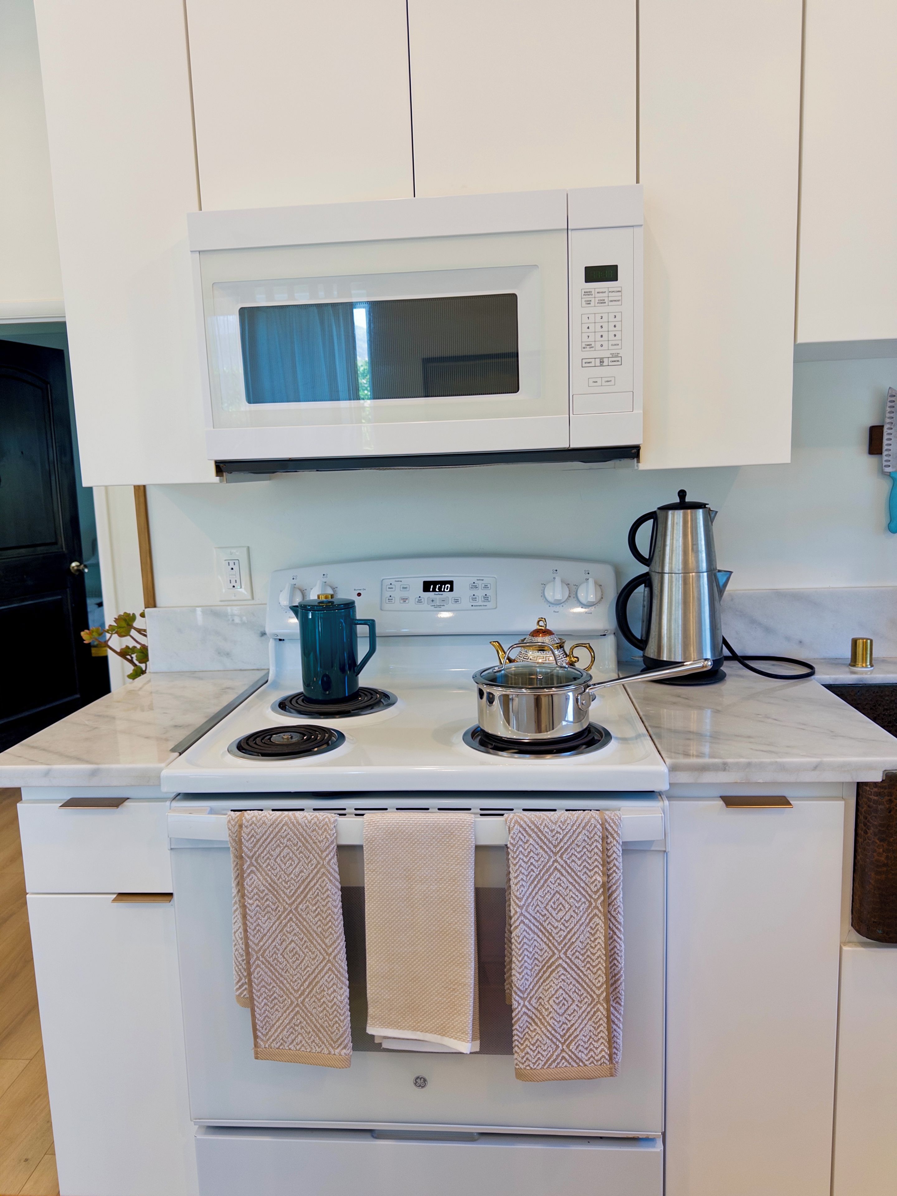 A kitchen with a microwave, stove, kettle, and a coffee pot.
