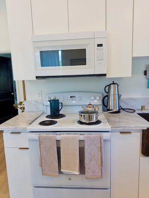 A kitchen with a microwave, stove, kettle, and a coffee pot.