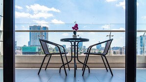 Ein Balkon mit Tisch und zwei Stühlen, einer Blumenvase und Blick auf die Stadt.