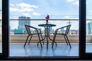 A balcony with a table and two chairs, a vase with flowers, and a cityscape view. - 3-bedroom apartment in Westlands perfect Family friendly retreat, Pool, Gym, Wow (Nairobi)