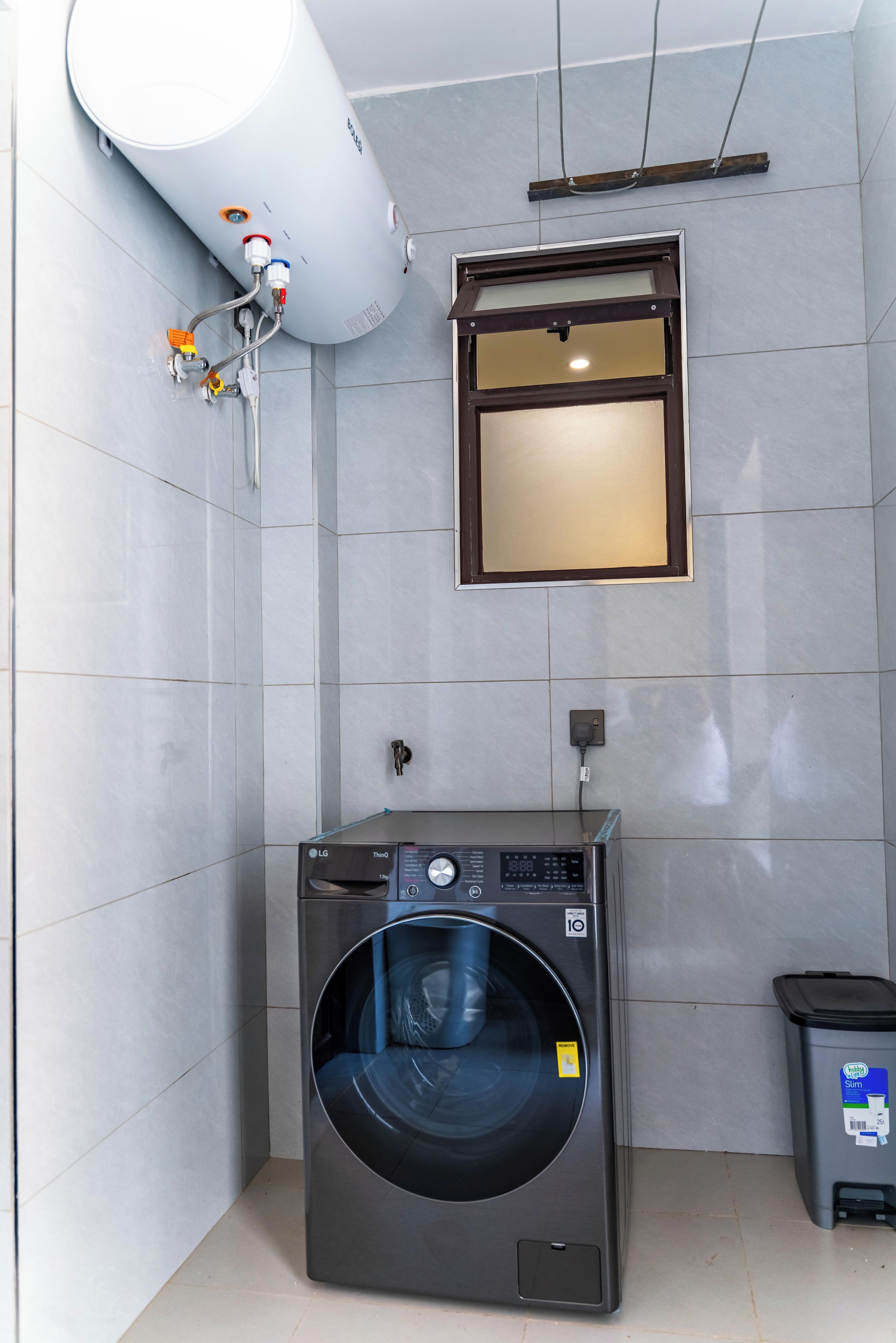 A laundry area with a washing machine, a water heater, and a trash bin.