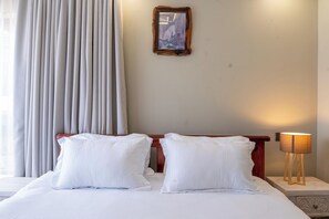 A hotel room with a bed, a nightstand, a lamp, a window with curtains, and a framed picture on the wall. - 3-bedroom apartment in Westlands perfect Family friendly retreat, Pool, Gym, Wow (Nairobi)