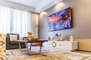 Un salon moderne avec un téléviseur à écran plat fixé au mur, un canapé gris, une table basse en bois et un vase décoratif avec des fleurs.