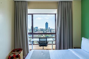 Une chambre d’hôtel avec un lit, une table et une chaise, et une vue sur le paysage urbain par une grande fenêtre.