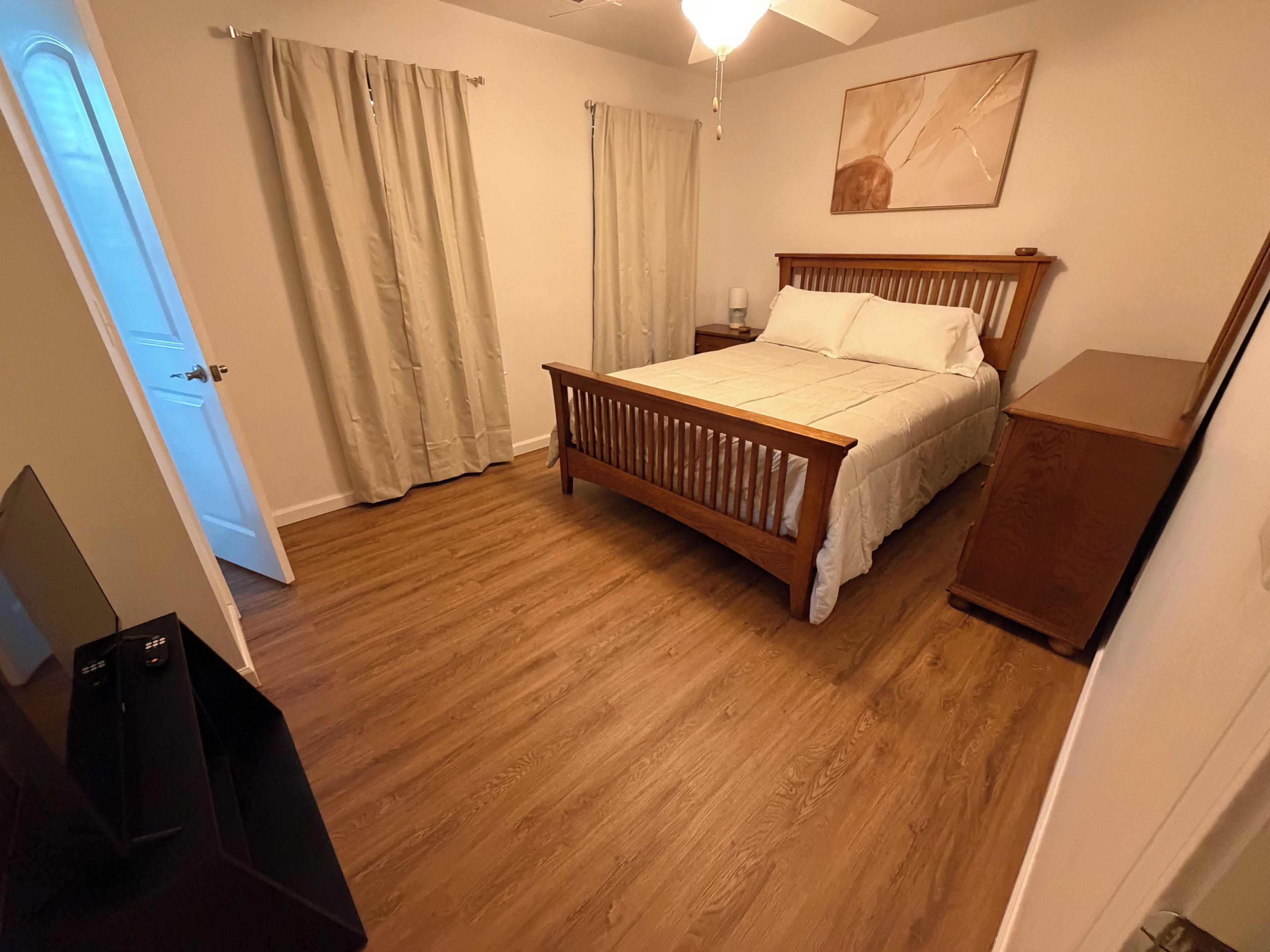 Une chambre à coucher avec un lit en bois, une table de chevet, une commode et un ventilateur de plafond.