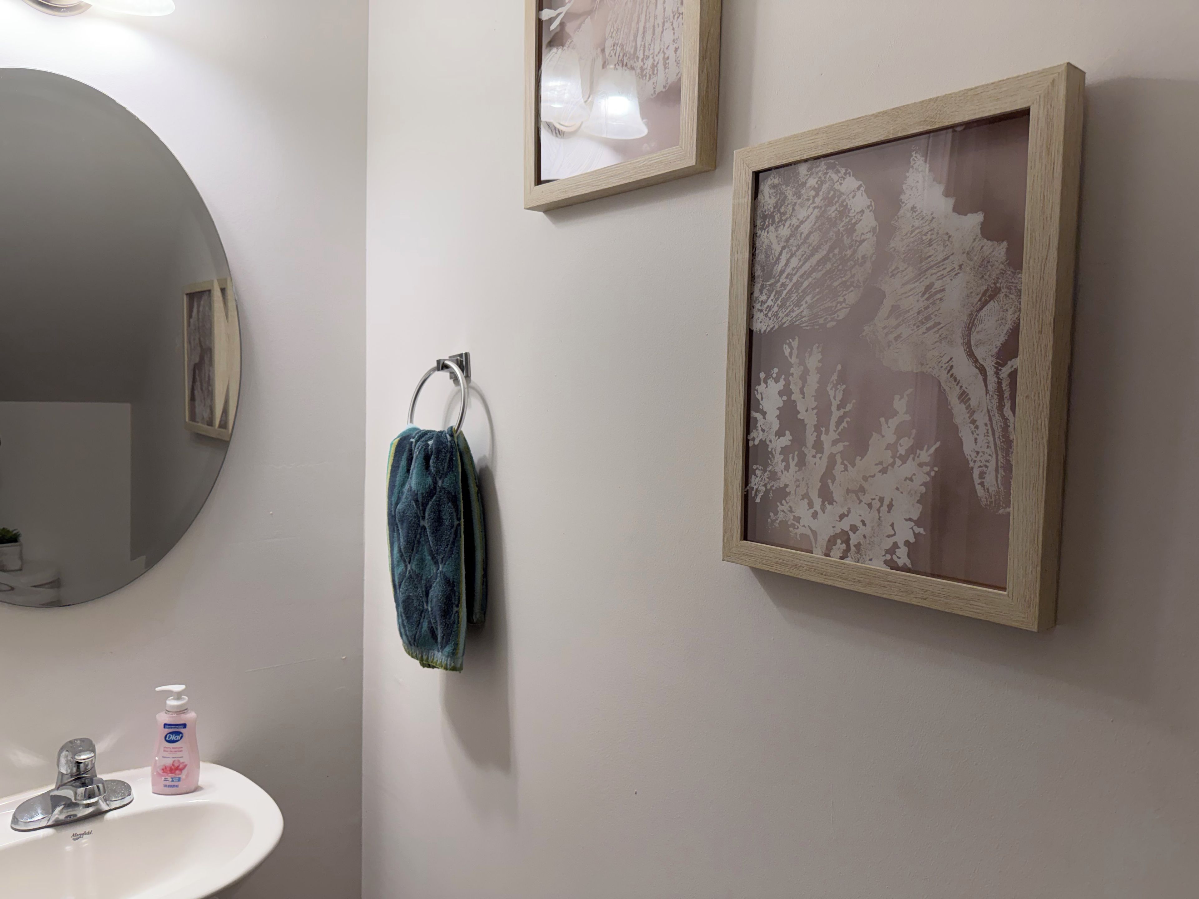 A bathroom with a round mirror, a sink with a faucet, a towel hanging on a metal ring, and two framed artworks on the wall.