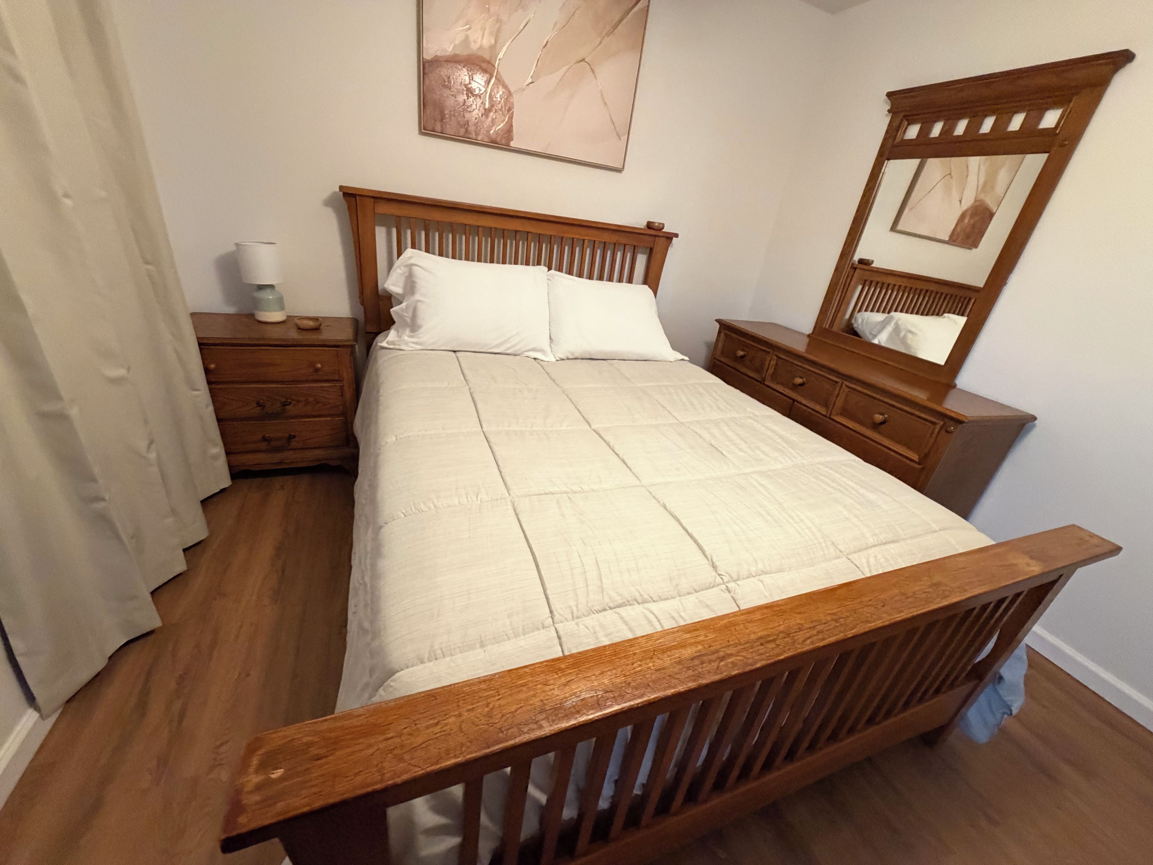 A bedroom with a wooden bed, a nightstand, a dresser, and a mirror.