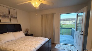 Ein Schlafzimmer mit einem Bett, einem Nachttisch, einer Lampe, einem Deckenventilator und einer Tür, die auf einen Balkon führt.