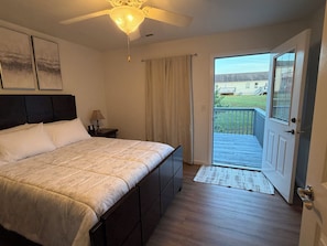 Ein Schlafzimmer mit einem Bett, einem Nachttisch, einer Lampe, einem Deckenventilator und einer Tür, die auf einen Balkon führt.