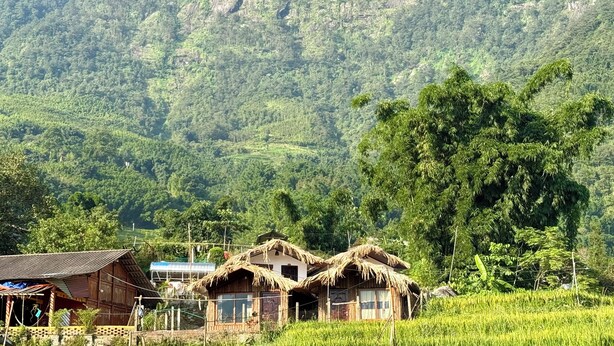 Un pueblo rural con casas tradicionales de techos de paja, rodeado de abundante vegetación y campos en terrazas.