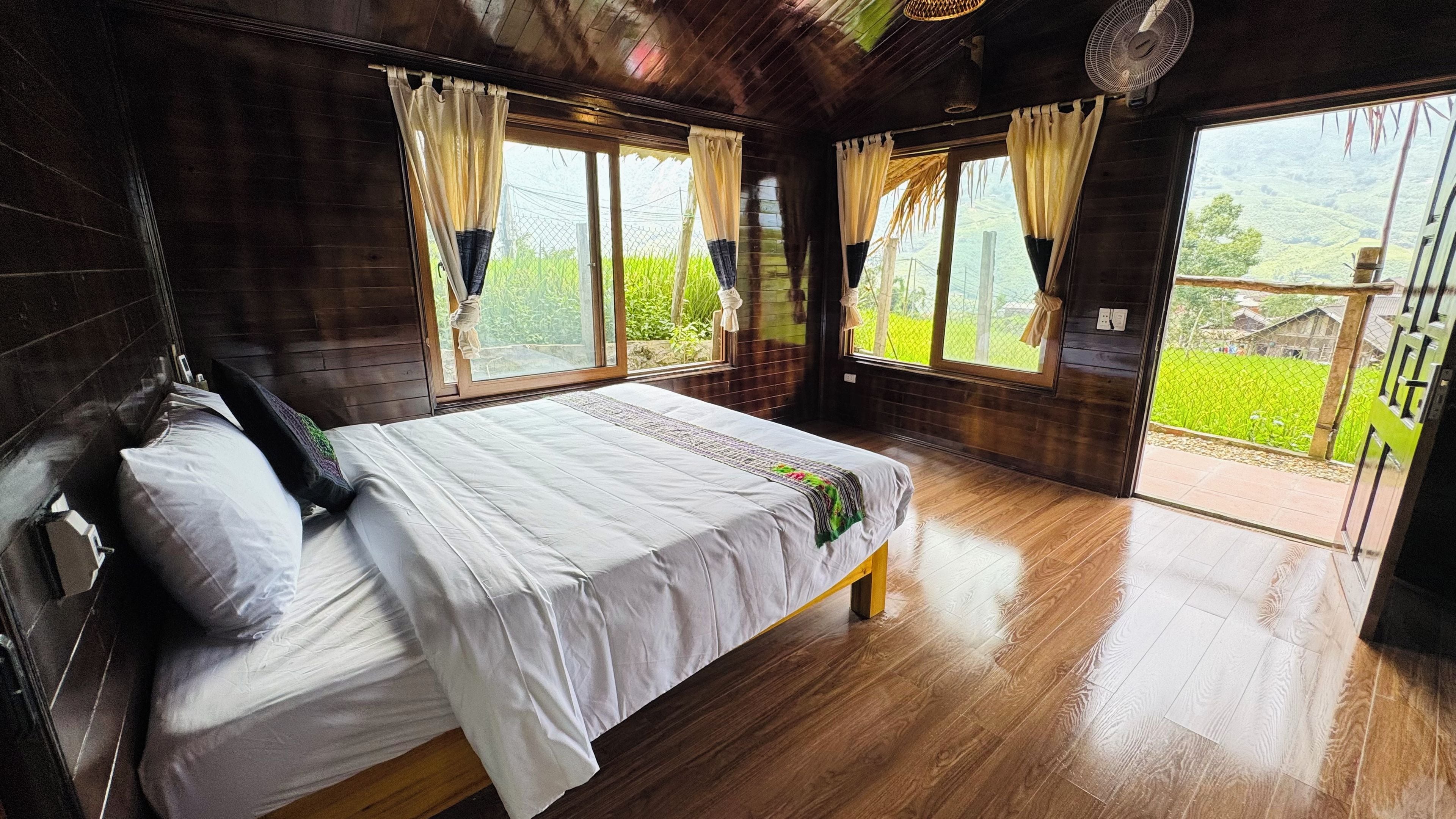 Una habitación de madera con una cama, ventanas amplias y vistas a zonas verdes.