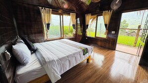 Una habitación de madera con una cama, ventanas amplias y vistas a zonas verdes.