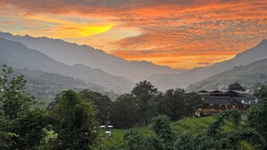 Un paisaje montañoso con un atardecer, un valle con vegetación y un edificio de diseño tradicional.