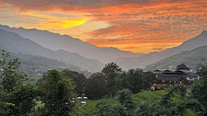 Un paisaje montañoso con un atardecer, un valle con vegetación y un edificio de diseño tradicional.