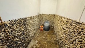 Un espacio reducido y cerrado con pared de guijarros, un bote de basura y un dispensador de agua.