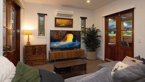 A living room with a television, wooden furniture, a potted plant, and a view through a glass door.