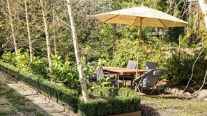 A patio with a table and chairs, surrounded by greenery and trees.