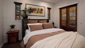 A bedroom with a bed, a nightstand, a potted plant, a framed artwork, and a wooden door. - Kingsleigh Daylesford (Daylesford)