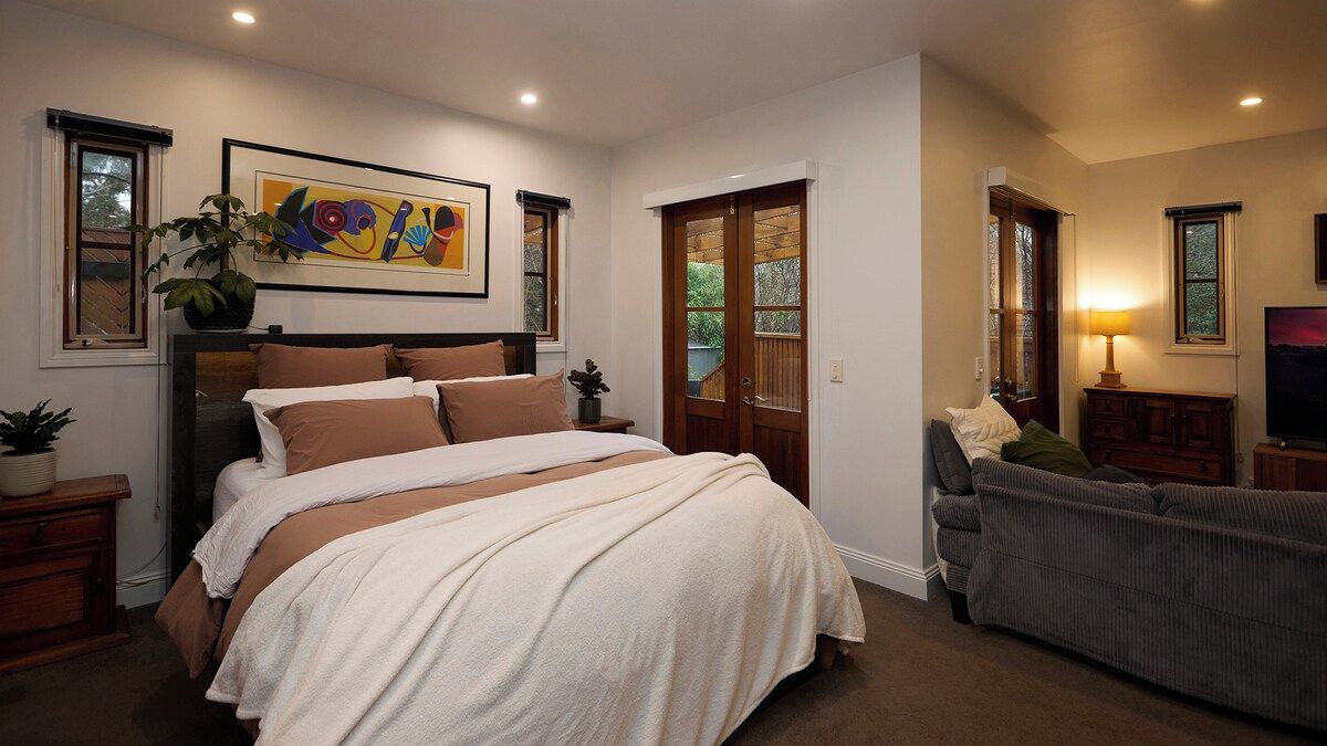 A bedroom with a large bed, a dresser, a nightstand, a potted plant, and a painting on the wall.