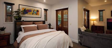 A bedroom with a large bed, a dresser, a nightstand, a potted plant, and a painting on the wall.